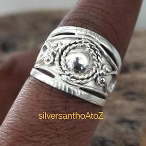 May include: A close-up of a silver ring with an intricate design. The ring features a central circular element surrounded by a rope-like pattern and decorative swirls. The ring is on a finger, and the text "silversanthoAtoZ" is visible.