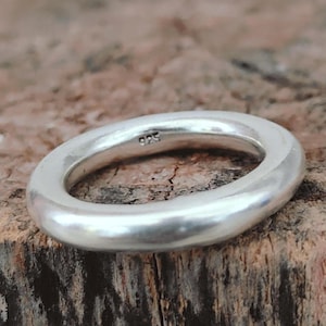 Op de afbeelding: Een zilveren ring met een glad, afgerond ontwerp. De ring is gemaakt van een glanzend, metalen materiaal en heeft een eenvoudige, elegante stijl. De ring is gemarkeerd met "925".