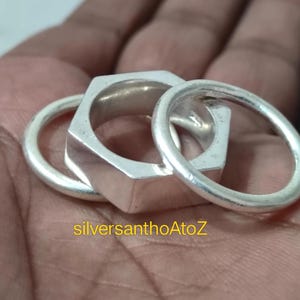 Könnte beinhalten: Ein Satz von drei silbernen Ringen, einer sechseckigen und zwei kreisförmigen. Die Ringe bestehen aus glänzendem Metall und sind zusammen angeordnet. Der Text "silversanthoAtoZ" ist in Gelb sichtbar.