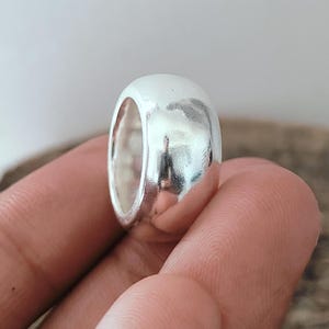 Könnte beinhalten: Nahaufnahme eines silbernen Rings mit rundem, glattem Design. Der Ring ist stark reflektierend und zeigt Licht und Schatten. Der Ring ist ein schlichtes, aber elegantes Schmuckstück.
