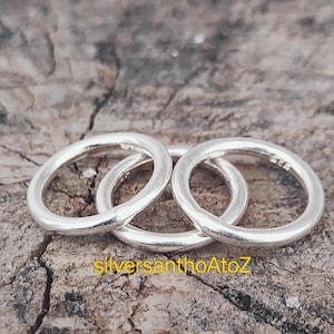 May include: Three silver rings interlocked, displayed on a textured, brown surface. The rings have a smooth, polished finish. The text "silversanthoAtoZ" is visible at the bottom.