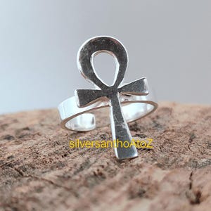 Könnte beinhalten: Ein verstellbarer Ring in Silber mit einem Ankh-Symbol. Der Ring befindet sich auf einer strukturierten, braunen Oberfläche. Der Text "silversanhoAtoZ" ist sichtbar.