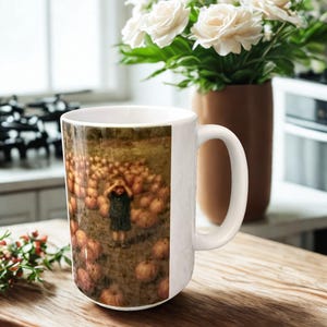 May include: White ceramic mug featuring a surreal image of a person standing in a field of pumpkins. The mug has a curved handle and is set on a wooden surface. A vase of white roses is in the background.