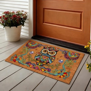 以下が含まれることがあります： カラフルなフクロウのデザインが施された長方形のドアマット。 フクロウは、青、オレンジ、緑、黄色の幾何学模様で描かれています。 マットは天然繊維でできており、木製のドアの前に置かれています。