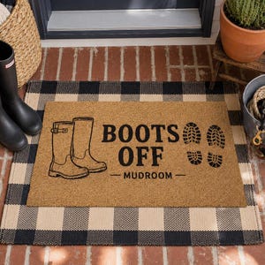 May include: A rectangular tan coir doormat featuring a black graphic of two tall boots, the text BOOTS OFF MUDROOM, and two boot print outlines. The mat is layered over a black and white buffalo check rug with a grid pattern design.
