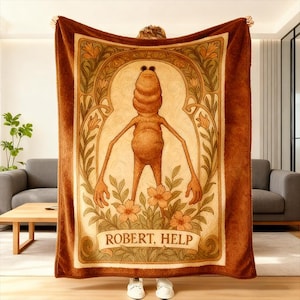 Puede incluir: Una manta de felpa marr&oacute;n con una figura de dibujos animados y el texto "ROBERT, HELP". La figura tiene un cuerpo bulboso, brazos largos y est&aacute; rodeada de elementos florales y de estilo art nouveau. La manta es de color marr&oacute;n c&aacute;lido.