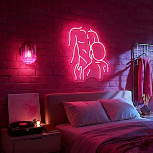 May include: A neon pink sign showing two figures, one larger and one smaller, on a brick wall. A pink wall sconce with a light bulb is to the left. The scene includes a bed with pink bedding, a record player, and a bedside table.