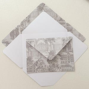 Könnte beinhalten: Weiße Umschläge mit einem grauen Toile-de-Jouy-Muster. Das Muster zeigt eine detaillierte Illustration einer Landschaft mit Gebäuden, Bäumen und Toren. Die Umschläge sind geöffnet und zeigen das gemusterte Innere und einen kleineren Umschlag.