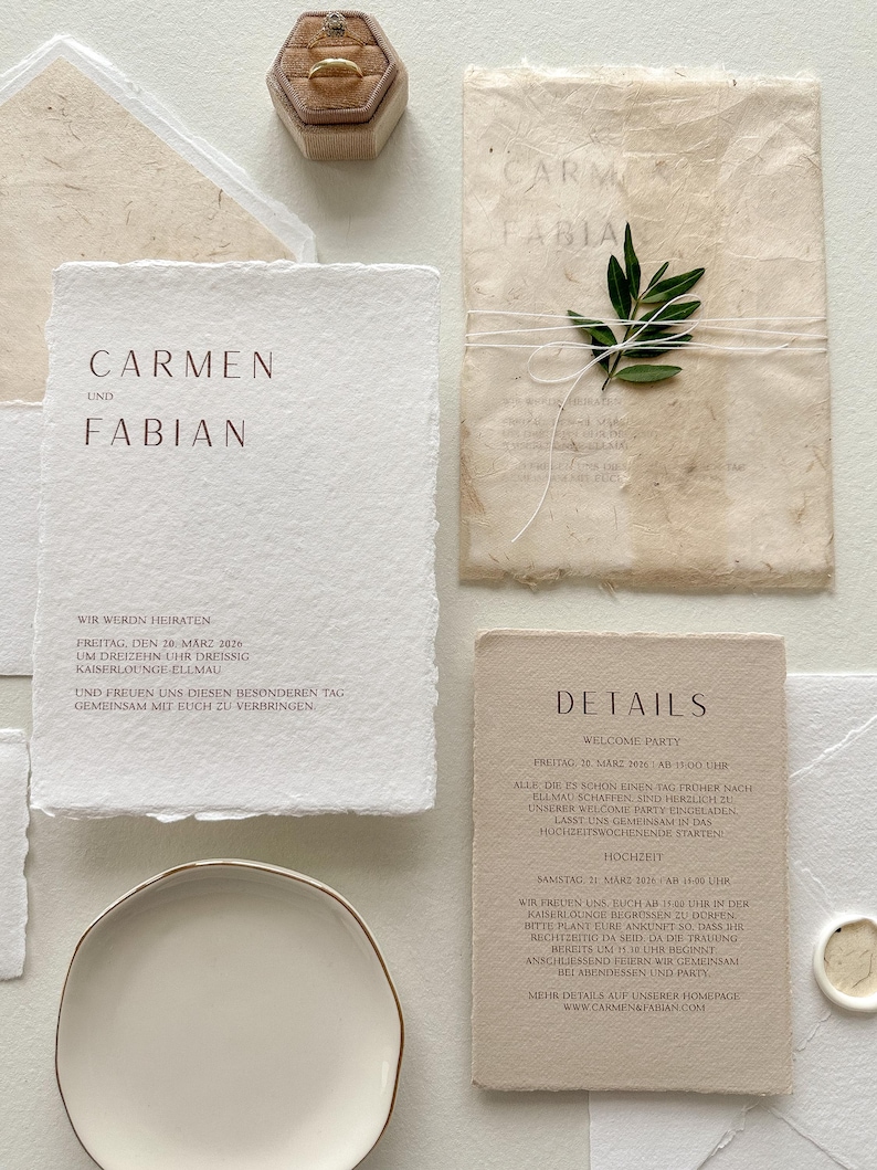 Pu&ograve; includere: Elegante suite di inviti di nozze con carta fatta a mano con testo in rilievo marrone. Include un portagioie, un rametto di verde e un piattino. Il testo recita "Carmen und Fabian" e i dettagli del matrimonio.