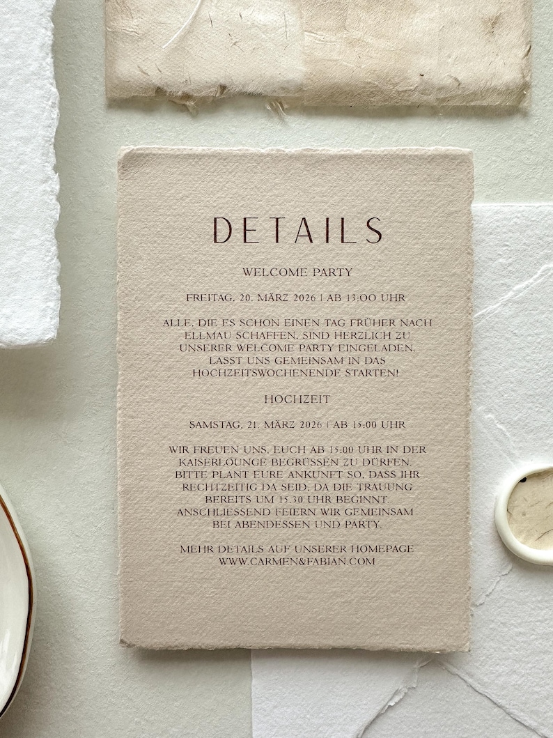 Pu&ograve; includere: Un biglietto d'invito beige con la parola "DETAILS" in un carattere marrone scuro. Il biglietto include il testo su una festa di benvenuto e i dettagli del matrimonio, con date e orari. Il biglietto &egrave; circondato da carta strutturata.