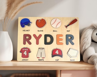 May include: Wooden baseball-themed puzzle with the name "RYDER" in colourful letters. Includes baseball equipment illustrations: helmet, glove, ball, bat, jersey, trousers, cap, and base. A decorative item for a child's room.