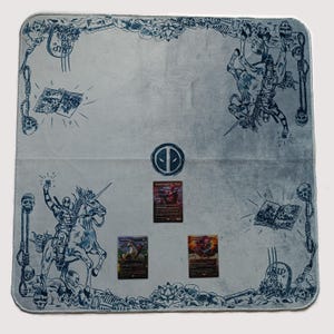 May include: A light blue playmat featuring Deadpool-themed illustrations and a central Deadpool logo. The border includes skulls, bones, and comic book imagery. Three trading cards are visible on the mat.