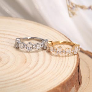 Könnte beinhalten: Zwei Klapp-Creolen, eine aus silberfarbenem und eine aus goldfarbenem Metall, jeweils mit einer Reihe abwechselnd im Baguette- und Rundschliff facettierter, klarer Steine, die entlang der Vorderseite des Rings angeordnet sind.