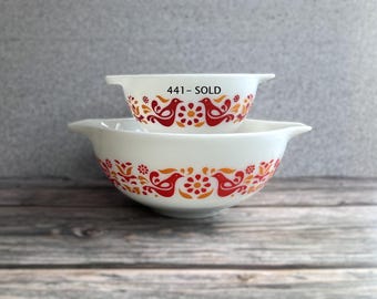 May include: Two white glass mixing bowls with side handles, featuring a repeating pattern of red and orange birds and floral motifs. The smaller bowl has the text 441 - SOLD printed in black on the front surface above the bird design.