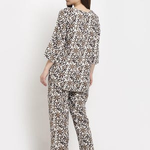 May include: A two-piece pajama set featuring a floral pattern in brown and black on a white background. The top has a round neck and three-quarter sleeves. The pants are straight-legged.