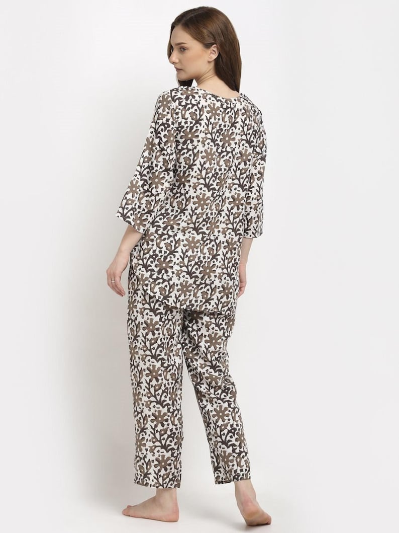 May include: A two-piece pajama set featuring a floral pattern in brown and black on a white background. The top has a round neck and three-quarter sleeves. The pants are straight-legged.