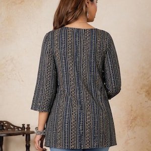 Pu&ograve; includere: Una tunica blu scuro caratterizzata da un motivo verticale di disegni geometrici e a forma di foglia color oro. Il capo presenta maniche a tre quarti e uno scollo rotondo, abbinato a jeans in denim di colore azzurro.