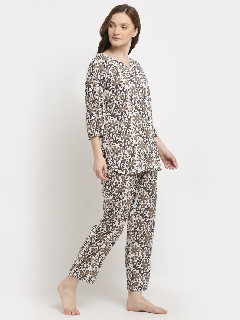 May include: A two-piece pajama set featuring a floral pattern in shades of brown and white. The top has a V-neck and three-quarter sleeves. The pants are long and straight-legged. The fabric appears to be lightweight and comfortable.
