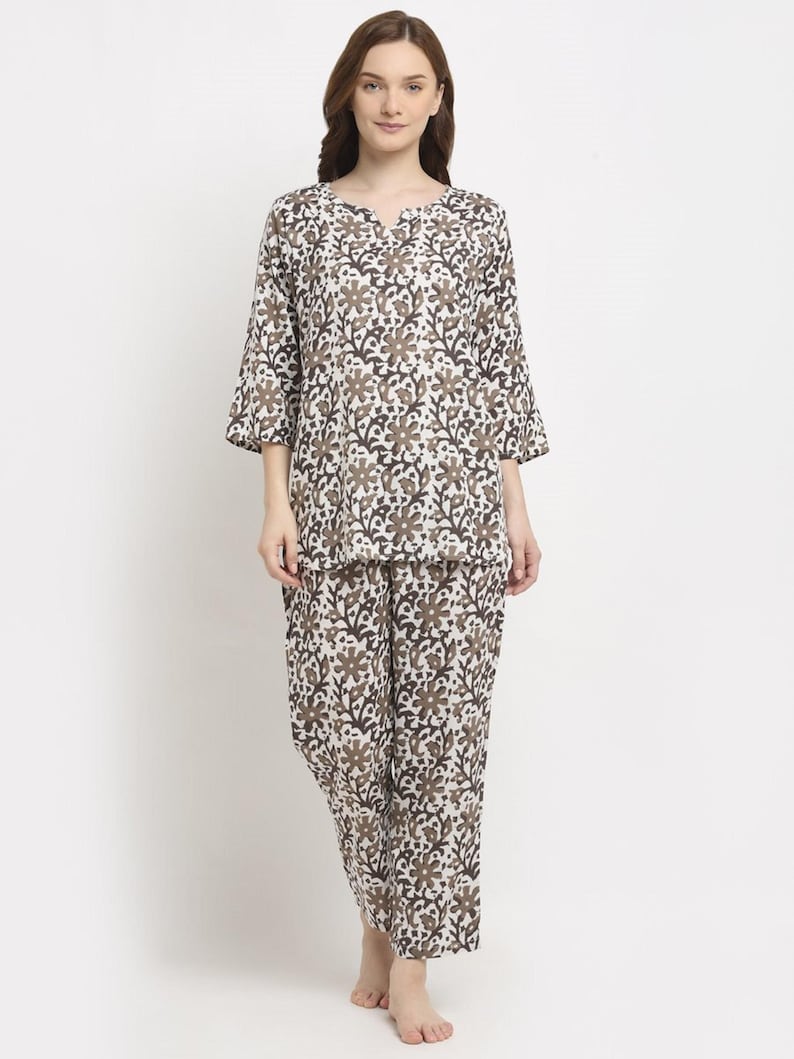 May include: A two-piece pajama set featuring a floral pattern in shades of brown and white. The top has a v-neck and three-quarter sleeves. The matching pants are loose-fitting.