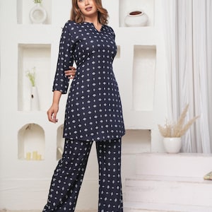 Op de afbeelding: Marineblauwe tweedelige outfit met een ruitpatroon. De top heeft een V-hals en driekwartmouwen. De broek met wijde pijpen past bij het patroon van de top. De outfit wordt gedragen met sandalen.