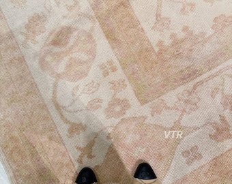 May include: A cream, peach, and tan floral patterned rug, with a central design and border. The image shows a person's feet wearing beige flats with black caps. The rug's design evokes a vintage aesthetic, suitable for home decor.