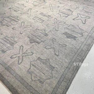 May include: A large, rectangular area rug in shades of gray. The rug features a repeating pattern of geometric shapes, including crosses and star-like figures. The border is a darker shade of gray, creating a defined edge.