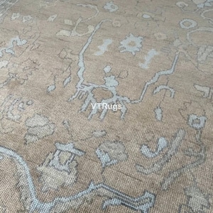 May include: Close-up of a beige rug with a detailed pattern in light blue and brown. The rug has a textured surface and a traditional design, suitable for home decor.