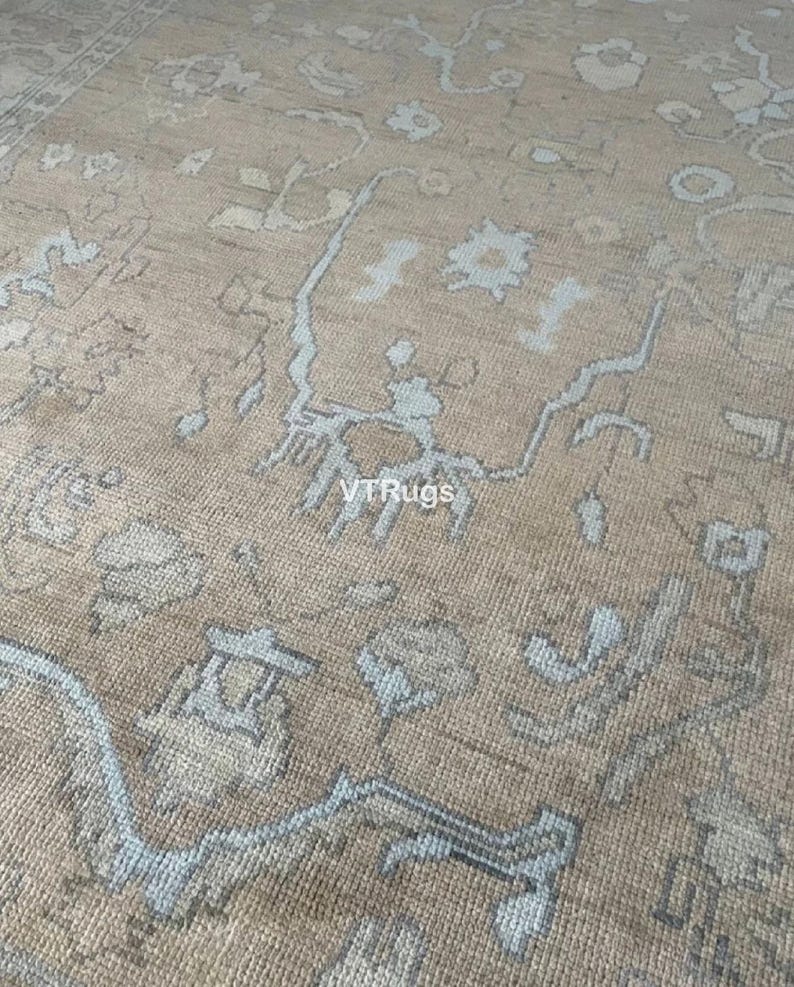 May include: Close-up of a beige rug with a detailed pattern in light blue and brown. The rug has a textured surface and a traditional design, suitable for home decor.