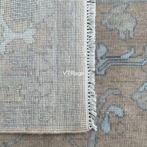 May include: Close-up of a beige and blue area rug with a floral pattern. The rug has a fringe edge and the text "VTRugs" is visible. The rug's design features light blue and beige floral motifs.