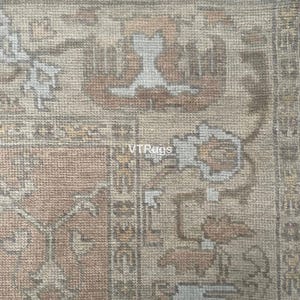 May include: Close-up of a section of a rug with a detailed, ornate pattern. The rug features a color palette of muted tones, including beige, peach, and gray. The design includes floral and geometric elements. The text "VTRugs" is visible.