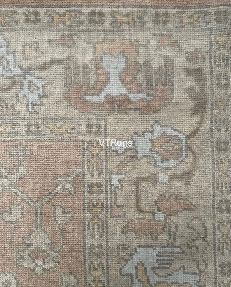 May include: Close-up of a section of a rug with a detailed, ornate pattern. The rug features a color palette of muted tones, including beige, peach, and gray. The design includes floral and geometric elements. The text "VTRugs" is visible.