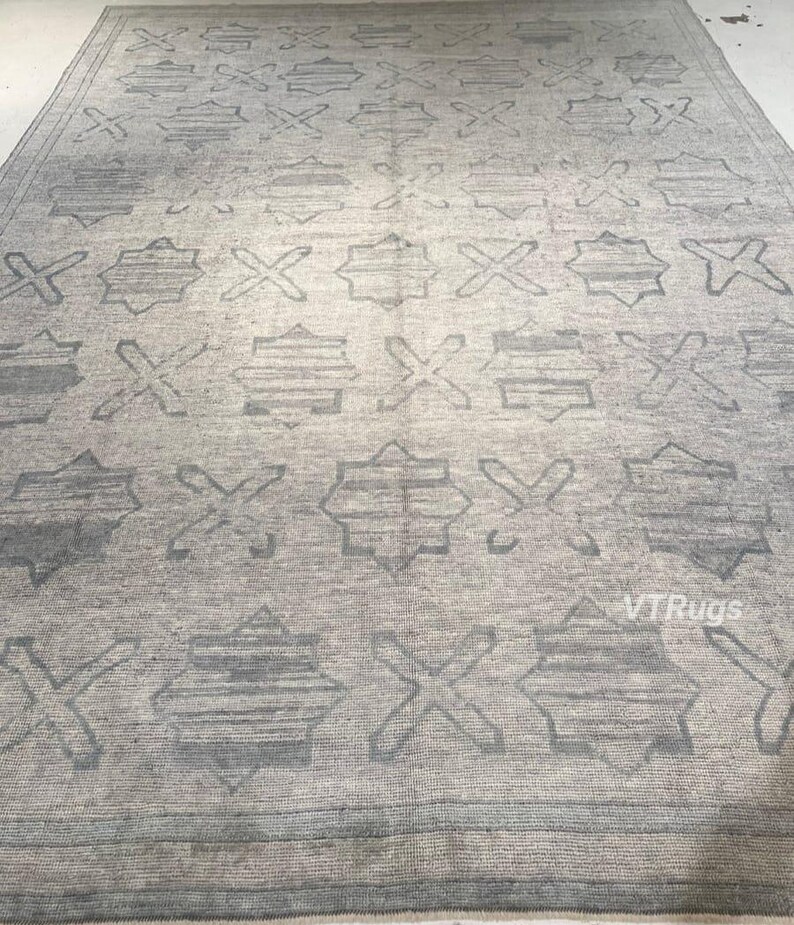 May include: A large, rectangular area rug in shades of gray. The rug features a repeating pattern of geometric shapes, including crosses and star-like designs. The overall design is symmetrical and the rug appears to be made of a woven material.