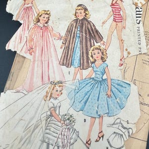 May include: Vintage paper doll wardrobe featuring illustrations of dolls in various outfits, including a pink gown, a brown cape, a blue dress, and a striped swimsuit. The text reads "High Heel Figure Dolls' Wardrobe."