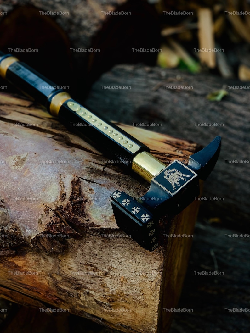 May include: A black and gold walking stick with a hammer-like head. The stick features gold accents and a decorative emblem on the head. The head has a cross design. The stick is resting on a wooden surface.