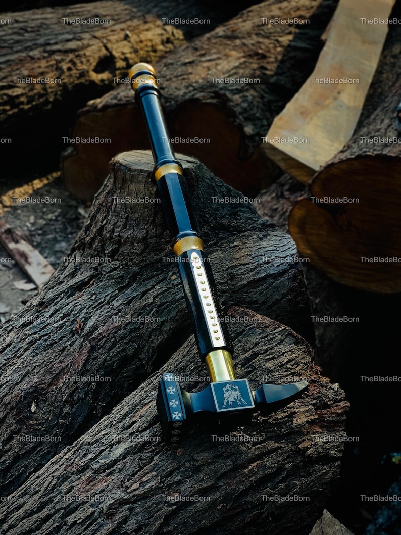 May include: A black and gold hammer with a long handle, resting on a pile of wood logs. The hammer head features a decorative emblem and cross symbols. The handle is black with gold accents.