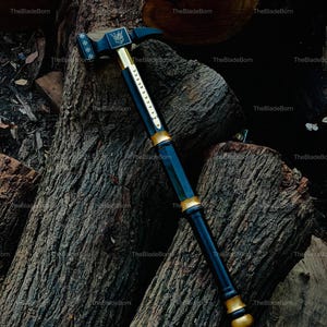 May include: A black and gold hammer with a decorative design. The hammer is resting on a pile of wood logs. The hammer has a black handle with gold accents and a gold head. The hammer's head has a decorative emblem.
