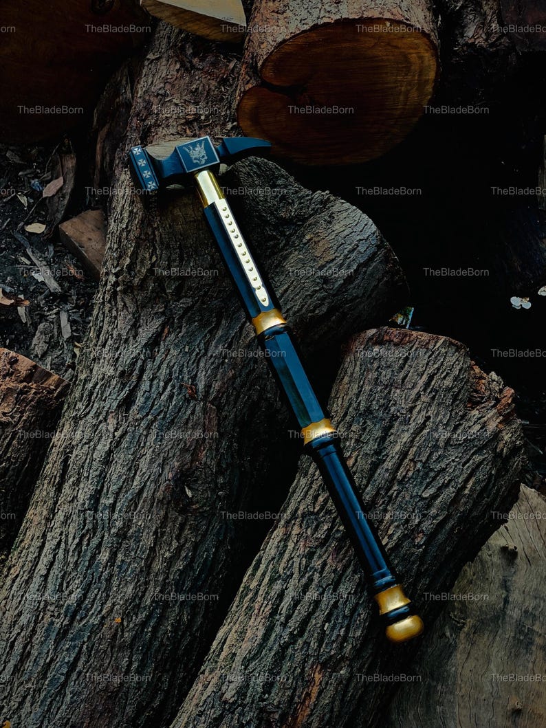 May include: A black and gold hammer with a decorative design. The hammer is resting on a pile of wood logs. The hammer has a black handle with gold accents and a gold head. The hammer's head has a decorative emblem.