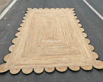 Könnte beinhalten: Ein rechteckiger Teppich aus naturfarbenen, gewebten Jutefasern. Der Teppich verfügt über einen markanten, wellenförmigen Rand mit einer dunkelgrünen Einfassung. Der Text FloorRugsDecor ist in Weiß in der Mitte der Teppichoberfläche aufgedruckt.