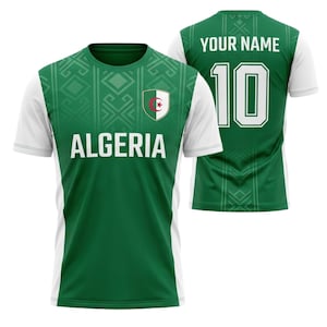 以下が含まれることがあります： 緑と白のサッカーユニフォーム。白のブロック体で「ALGERIA」の文字。アルジェリアの国旗と背番号10、名前を入れるスペースがあります。肩には幾何学模様が施されています。