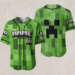 May include: Green baseball jersey with a pixelated design, featuring the word "NAME" in white block letters. The jersey has black trim and the number "00" on the front. The back of the jersey displays a black pixelated face.