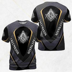 Pode incluir: Camiseta preta com um design maçónico. A camisa tem um padrão geométrico nos ombros e mangas, com um emblema central de um compasso e esquadro. A palavra "FREEMASON" é impressa verticalmente em ambos os lados do emblema.