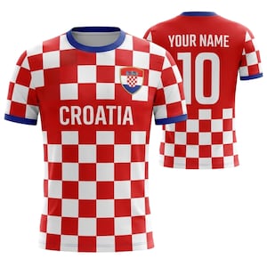 Op de afbeelding: Een rood-wit geblokt Kroati&euml; voetbalshirt met het woord "CROATIA" over de voorkant. Het shirt heeft een blauwe kraag en mouwboorden, en het Kroatische wapen staat op de borst. De achterkant is rood met nummer 10 en de tekst "YOUR NAME".