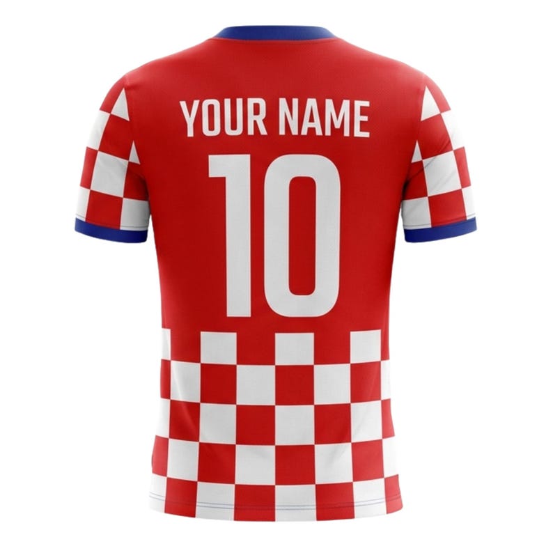Op de afbeelding: Rood voetbalshirt met een wit geblokt patroon aan de onderkant en mouwen. Het heeft een blauwe kraag en boord. Het nummer 10 is in het wit op de achterkant gedrukt, samen met de tekst "YOUR NAME".
