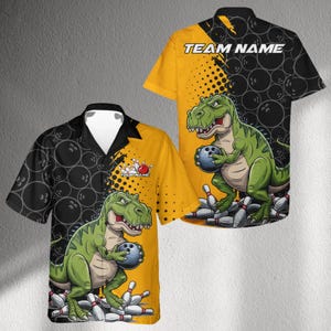 Puede incluir: Camisa de bolos de manga corta con un gráfico de dinosaurio de dibujos animados. La camisa presenta un T-Rex verde sosteniendo una bola de bolos, con bolos a sus pies. La camisa tiene un esquema de color amarillo y negro con el texto "TEAM NAME".