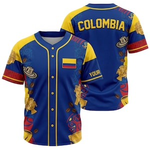 May include: A blue baseball jersey with yellow accents, featuring the word "COLOMBIA" on the back. The jersey has a button-up front and a small Colombian flag. It is decorated with coffee beans and gold-colored pre-Columbian art.
