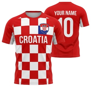 May include: A red and white checkered Croatia soccer jersey with the word "CROATIA" across the chest. The jersey has a Croatian coat of arms on the chest and the number 10 on the back. The back of the jersey also has the text "YOUR NAME".