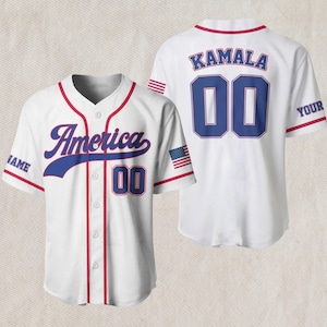 May include: White baseball jersey with red and blue detailing. The front says "America" in blue script and has the number "00". The back shows "KAMALA" and "00" in blue. An American flag patch is on the sleeve.