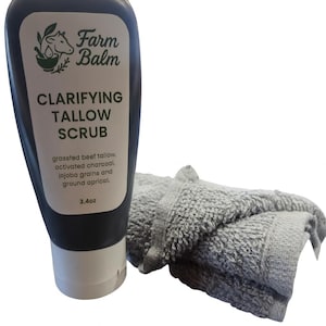 Könnte beinhalten: Eine dunkelgraue Flasche Farm Balm klärendes Talg-Peeling mit weißem Etikett und ein graues Waschtuch. Das Etikett enthält Produktname, Inhaltsstoffe und 96g.