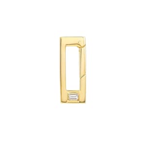 Puede incluir: Un cierre rectangular de color dorado con una pequeña gema rectangular y transparente engastada cerca de la parte inferior. El cierre está abierto, revelando un interior hueco. La joya está colocada sobre un fondo blanco.