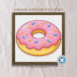 May include: A framed cross-stitch pattern of a pink frosted donut with colorful sprinkles. The donut has a yellow base and a pink frosting with blue and yellow sprinkles. The text "CROSS STITCH PATTERN" is at the top.